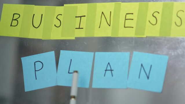Businesswoman in suit write business plan on Post-it sticky notes and paste on the board for business planning and marketing.