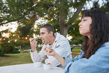 Couple eats fruit salad at picnic table in park