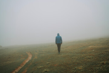 Man walking away on misty road.