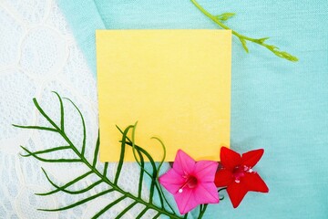 緑の布に白のレースを背景に赤とピンクの星型のルコウ草の花を添えた黄色のコメントスペースのモックアップ