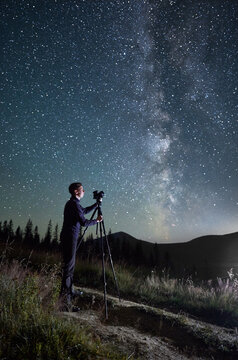 Professional photographer taking photos of Milky Way. Young male focusing his camera to take perfect picture of starry sky. Male taking pictures of night sky full of stars in mountains.