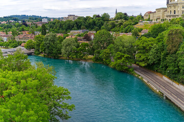 Fototapeta premium Scenic aerial view of Aare River with trees alongside urban road at Swiss City of Bern a cloudy summer day. Photo taken July 1st, 2023, Bern, Switzerland.
