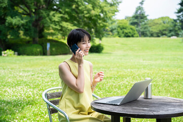 Young Asian businesswoman calling on smartphone while working outdoors on her laptop in an outdoor cafe.female entrepreneur running her own business. Business lifestyle and technology