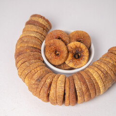 Figs or dried figs on white bowl with white background, Figs or dried figs arranged in round shaped on the white background in a wooden bowl. The fig is the edible fruit of Ficus Carica