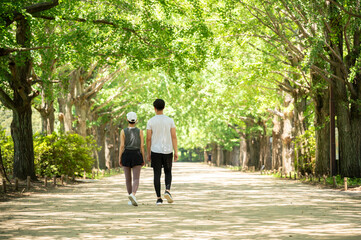 Young man and woman jogging along a tree-lined path in the park - obrazy, fototapety, plakaty