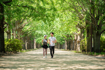 Young man and woman jogging along a tree-lined path in the park