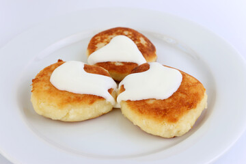 Delicious, ruddy cheesecakes covered with sour cream on a white plate.