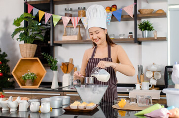Asian female baker bakery pastry chef wears white tall hat and apron standing smiling holding add...