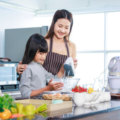 Asian female mother wears apron smiling teaching helping little girl daughter holding blender...