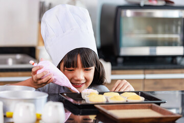 Closeup shot of Asian female little girl baker pastry bakery chef daughter wears white tall hat...
