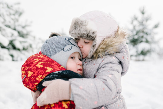 Kids hug and kiss in snow park. Children having fun and playing outdoors. Childs walking snowy mountains, time together. Winter holidays. Kids embrace, enjoying in winter forest. Frost winter season.
