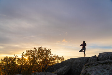 Woman doing yoga tree pose on top of a mountain at sunrise