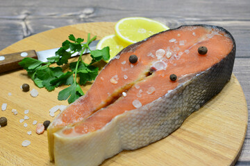 salmon steak with salt, parsley and lemon slices on the cutting board close up 