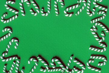 Flat lay Christmas composition with frame of candy canes on a green background. Copy space for text