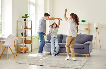 Full length portrait of a happy family of three having fun and dancing with a child girl in the living room at home. Portrait of young parents spending time with daughter. Family leisure concept.