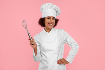 Naklejka premium Happy female chef in uniform holding whisk on pink background