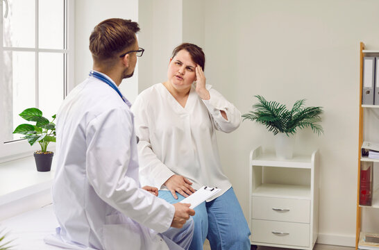 Young fat woman sitting on the couch in the doctor's office suffering from headache feel stressed, migraine or depression during medical examination in clinic. Health care and medicine concept.
