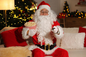 Merry Christmas. Santa Claus with popcorn bucket changing TV channels on sofa at home
