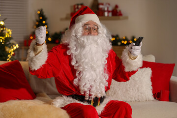 Merry Christmas. Santa Claus with remote control watching TV on sofa at home