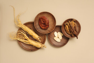 Top view of rare herbal displayed on wooden dishes - ginseng roots, ganoderma mushrooms and red ginseng. Beige background for advertising product and space for design
