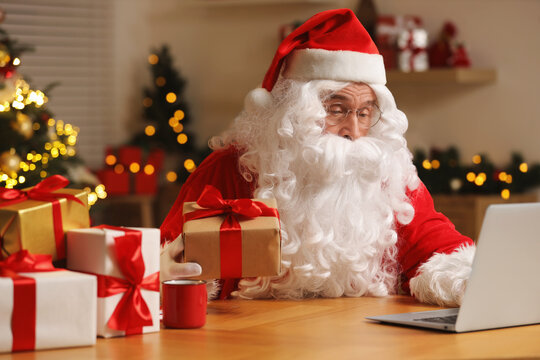 Santa Claus with Christmas gift using laptop at table in room