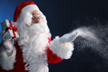 Santa Claus with Christmas gift blowing snow on dark blue background