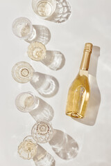 Summer party drinks flat lay, wine glasses with white sparkling wine and sunshine shadow on light...