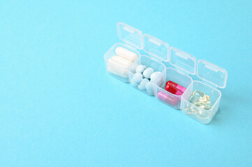 Medical pill box with a variety of different of tablets for daily take a medicine. On a light blue background.