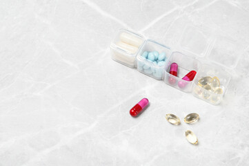 Medical pill box with a variety of different of tablets for daily take a medicine. On a light stone background.