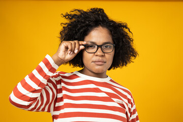 Curly young woman in glasses on yellow background