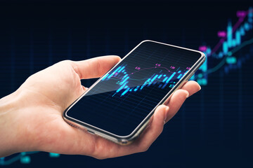 Close up of male hand holding mobile phone with glowing upward candlestick forex chart on dark grid...