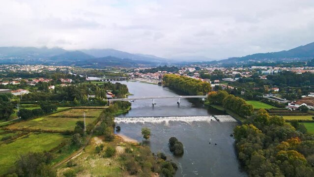 Stunning aerial 4K drone footage of a village - Ponte de Lima and its two bridges crossing over the Lima River. Filmed in autumn during partly cloudy weather.