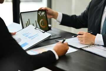 Finance investment analyst using digital tablet and analyzing sales statistics document at meeting