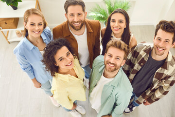 Fototapeta na wymiar Top view portrait of a group of young happy smiling friends students or colleagues in casual clothes standing together in at home and looking up confidently and positively at camera.