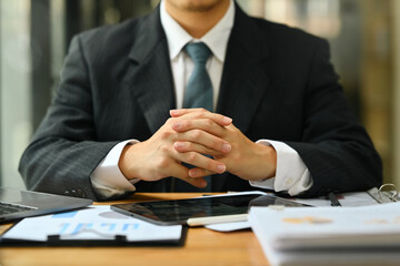 Unrecognizable businessman sitting at desk with hands clasped showing power and confidence