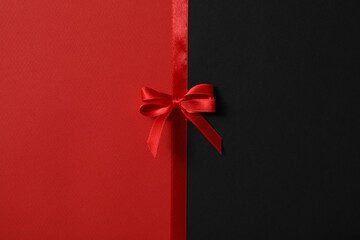 Red ribbon with bow on red and black background, top view