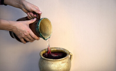 A hand holds a clay jar and pours water - obrazy, fototapety, plakaty