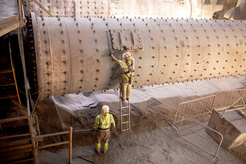 Workers are repairing the grinding mechanism in the workshop of a cement plant. Work technology,...
