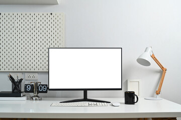 Modern workplace with blank computer monitor, coffee cup, lamp and peg board on wall