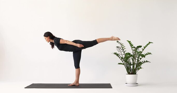 Yoga instructor performing exercises Virabhadrasana, warrior number three pose and Ardha Chandrasana, half moon pose, training in short leggings and a T-shirt while standing on a mat in the studio