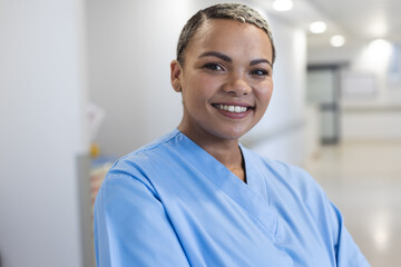 Portrait of happy biracial female doctor with short hair wearing scrubs in corridor at hospital
