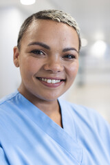 Portrait of happy biracial female doctor with short hair wearing scrubs in corridor at hospital