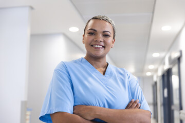 Portrait of happy biracial female doctor with short hair wearing scrubs in corridor at hospital - Powered by Adobe