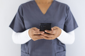 Midsection of biracial female doctor wearing scrubs using smartphon in hospital