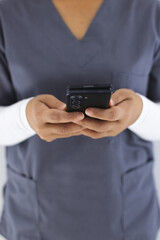 Midsection of biracial female doctor wearing scrubs using smartphon in hospital