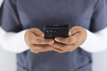 Midsection of biracial female doctor wearing scrubs using smartphon in hospital