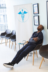 Thoughtful african american male doctor wearing scrubs sitting in waiting room in hospital