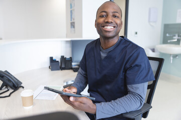 Portrait of happy african american male doctor using tablet at reception desk in hospital