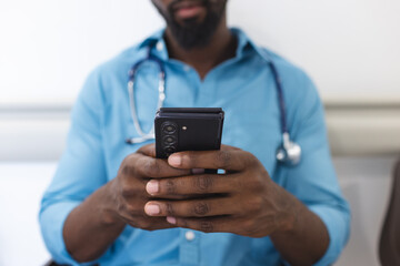 Midsection of african american male doctor using smartphone in waiting room in hospital