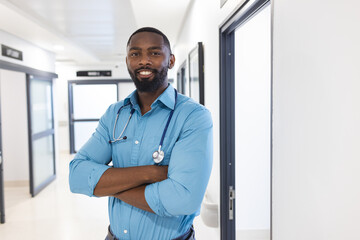 Portrait of happy african american male doctor in corridor in hospital, copy space